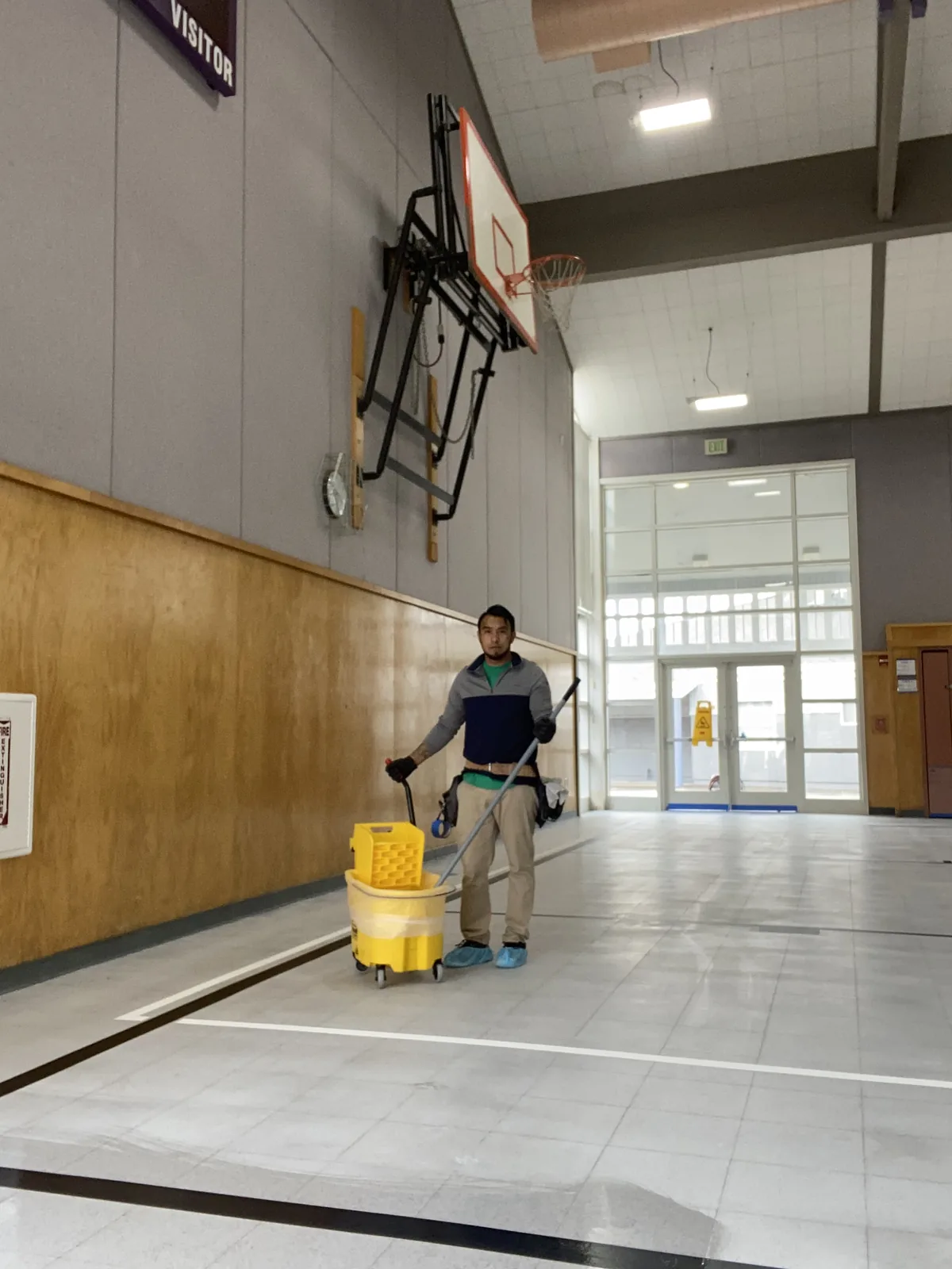 Technician mopping a gymnasium floor with a mop bucket